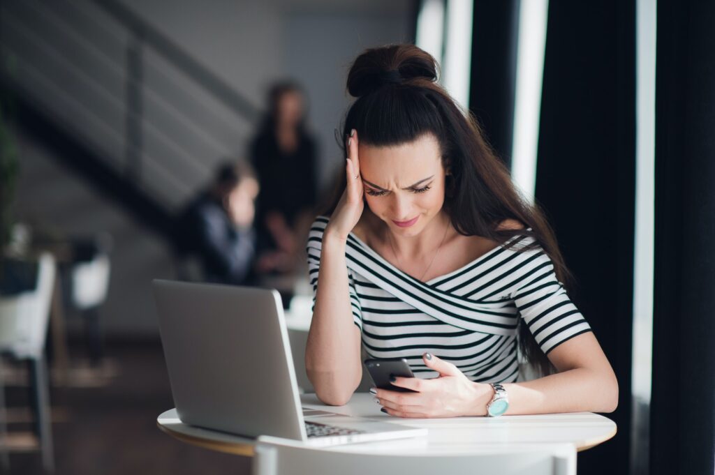 Portrait of stressed office young woman holding a cellphone in hands in a cafe, looking at the